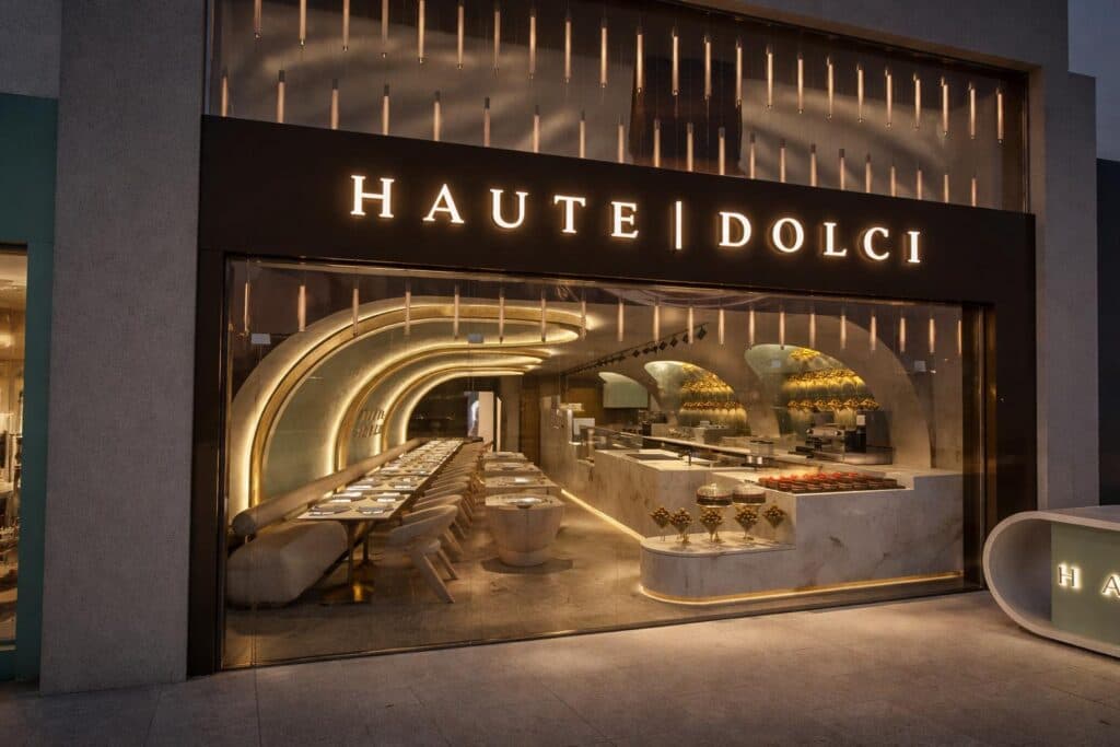 The illuminated Haute Dolci shopfront at dusk, looking through to the finished dining room